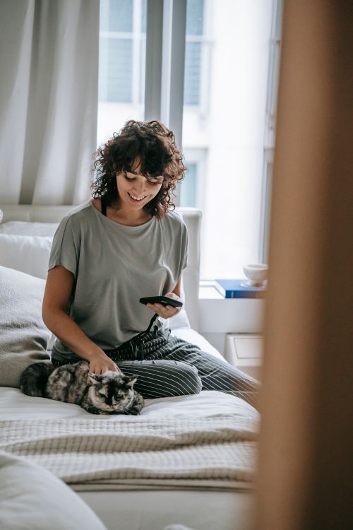 一位年輕女性在家中床上與貓咪互動